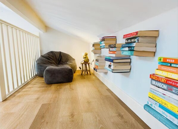 A cozy reading nook with a bean bag chair and a small table, a wall-mounted bookcase filled with books, and a radiator on the left.