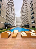 Una piscina con sillones de descanso al frente, rodeada de edificios residenciales altos.