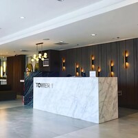 A modern reception desk with a marble top labeled "TOWER 1," a staircase, and a wall with vertical light fixtures.