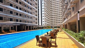 Una piscina con lettini e tavoli, circondata da edifici residenziali a più piani.