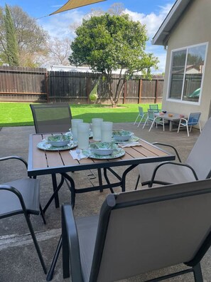 A patio with a table set for four, outdoor chairs, and a dining table with plates and cups. - Orange Blossom Bungalow - 2/2 Lush Yard+Kids Toys! (Vacaville)