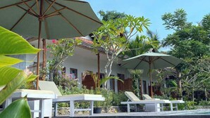A pool area with lounge chairs and umbrellas, surrounded by tropical plants and a building with a wooden structure. - Green Sunrise Hill View (Penida Island)