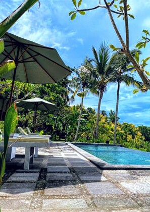 A pool area with lounge chairs and umbrellas, surrounded by palm trees and tropical vegetation. - Green Sunrise Hill View (Penida Island)
