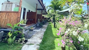 A traditional house with a covered porch, a concrete pathway, and lush greenery including flowering plants. - Green Sunrise Hill View (Penida Island)