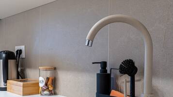 Una cocina moderna con un grifo curvo, una cafetera, un tarro de especias y un cepillo.