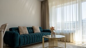 Un salón moderno con un sofá color turquesa, dos cojines color beige, una mesa redonda dorada y un jarrón con flores.