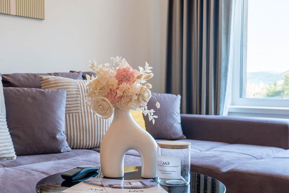 A modern living room with a sofa, a vase with flowers, a remote control, and a glass jar with a label.