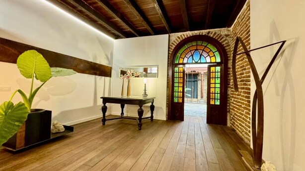 A hallway with wooden flooring, a bench, a potted plant, and a stained glass window.