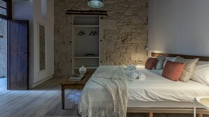 A bedroom with a stone wall, a wooden bed, a bedside table with books, and a hanging light fixture.