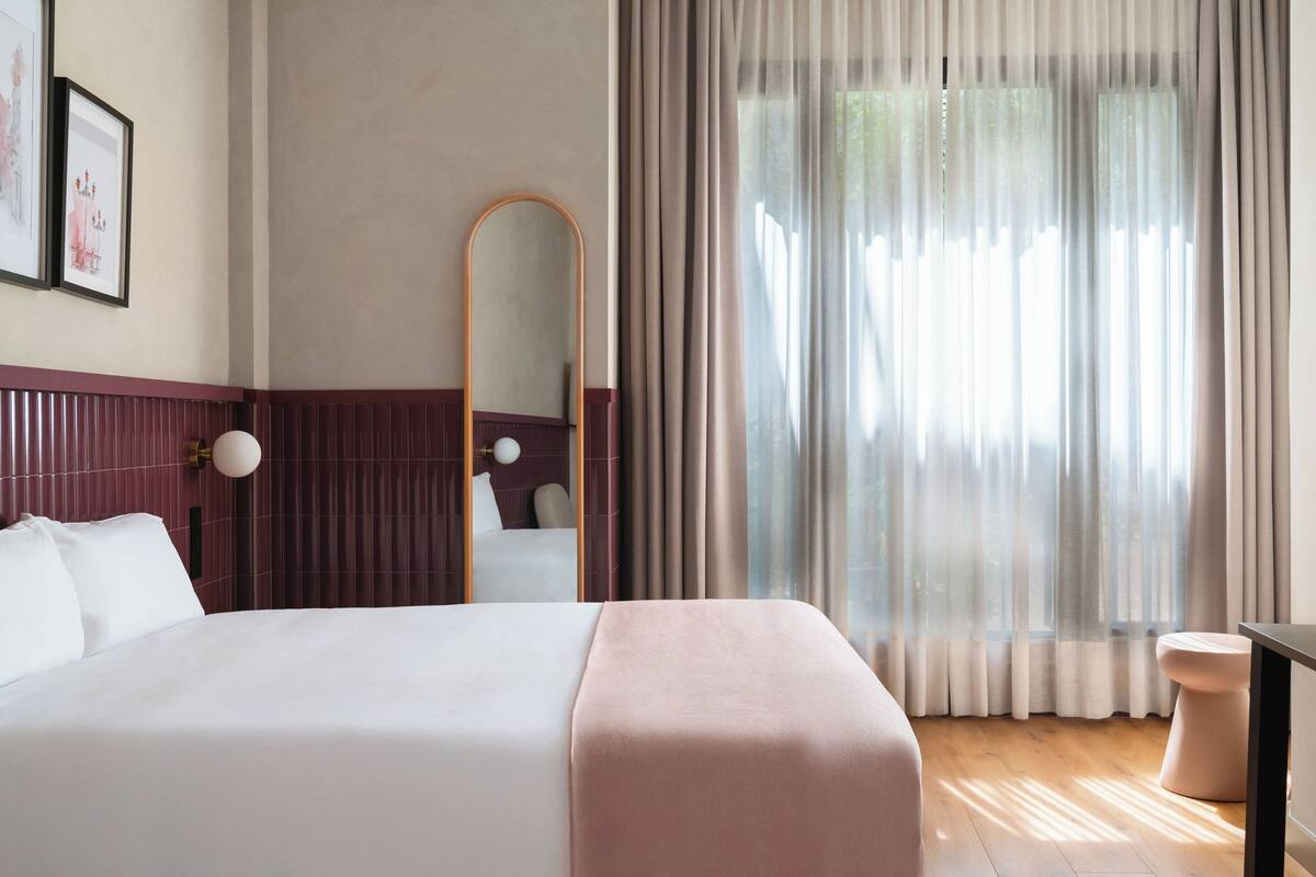 Una camera d'albergo con un letto grande, un comodino, uno specchio e una finestra con tende.