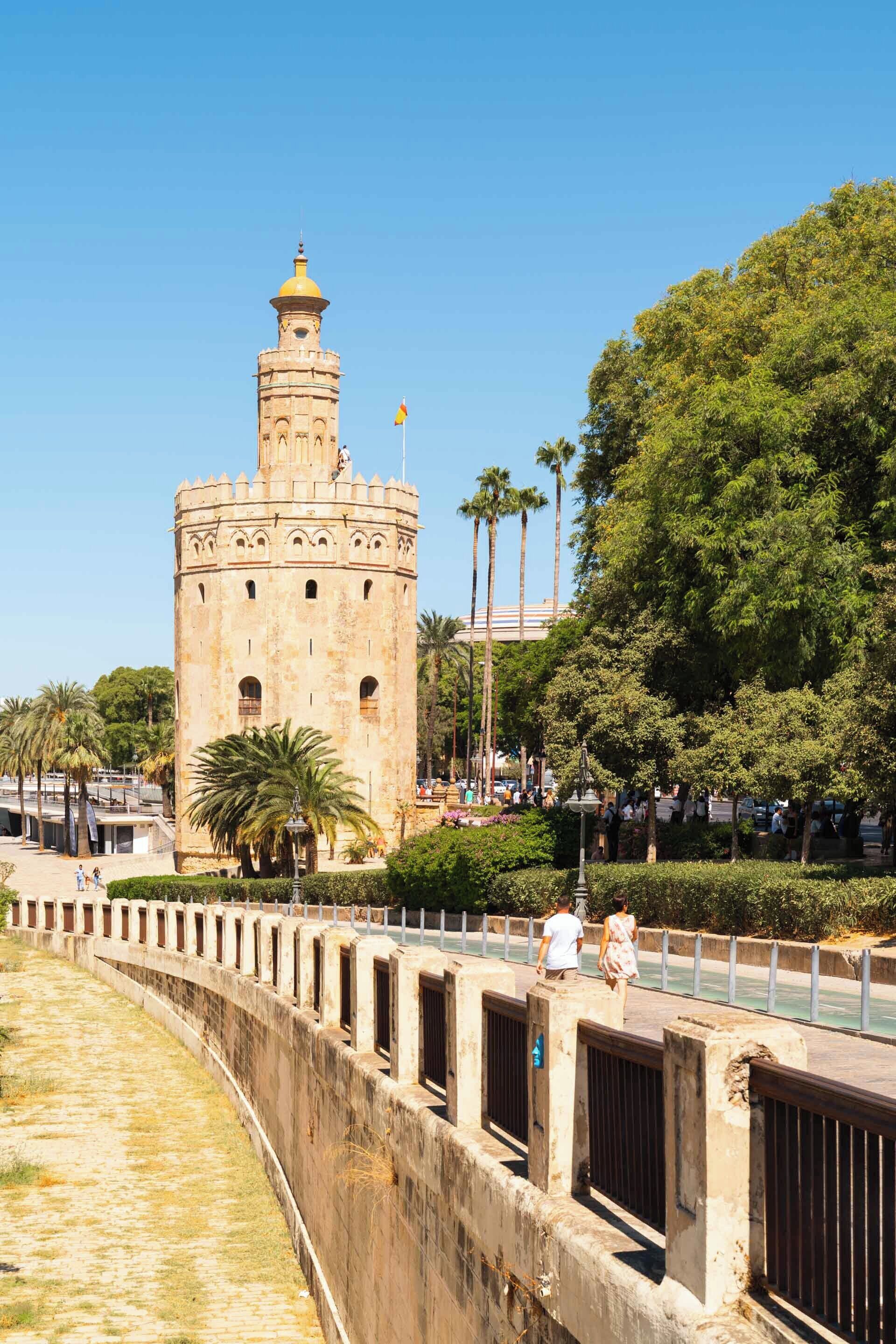 A historic tower with a dome, surrounded by greenery and palm trees.
