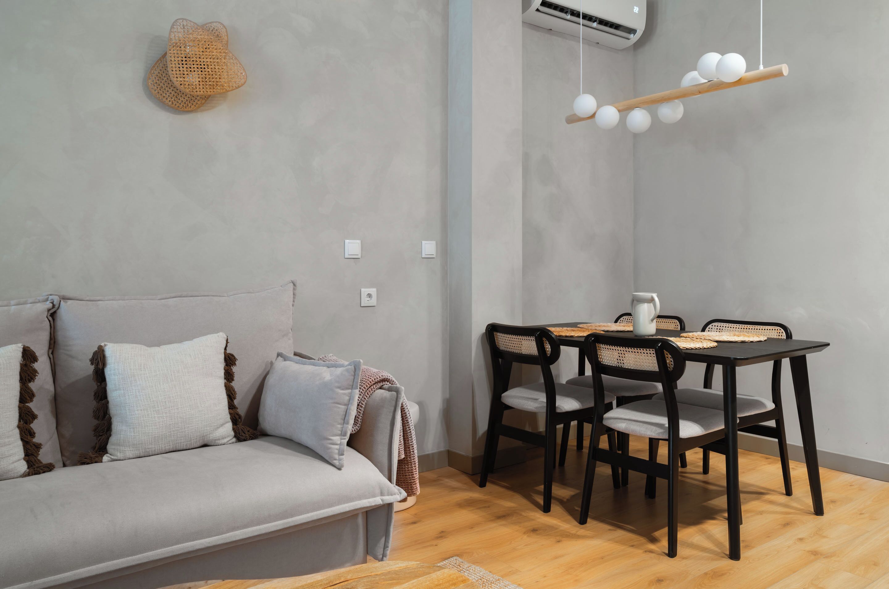 Een moderne woonkamer met een grijze bank, een eettafel met vier stoelen en een hanglamp.