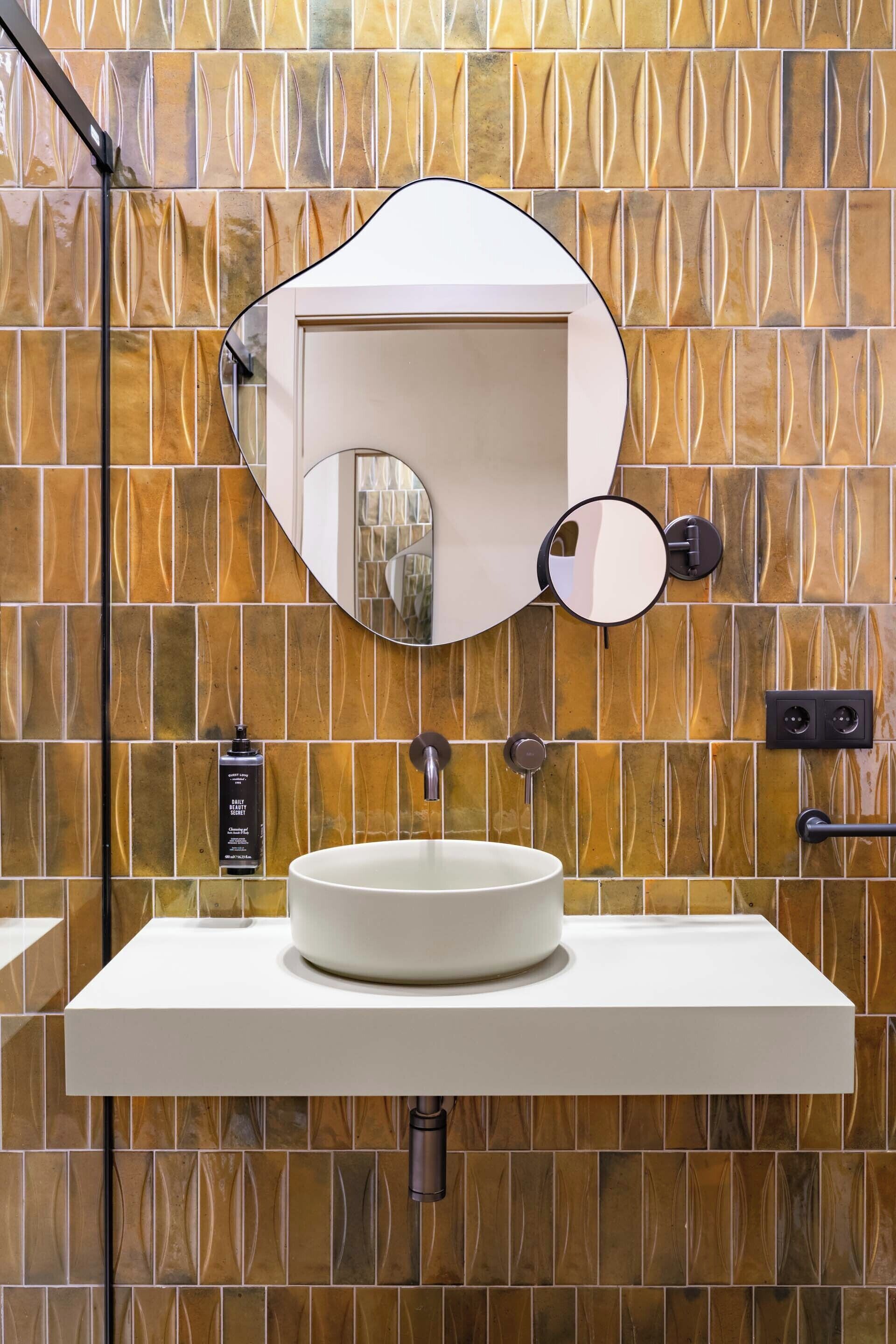 Un baño con un lavabo blanco, un espejo grande y una pared con diseño de baldosas estampadas.