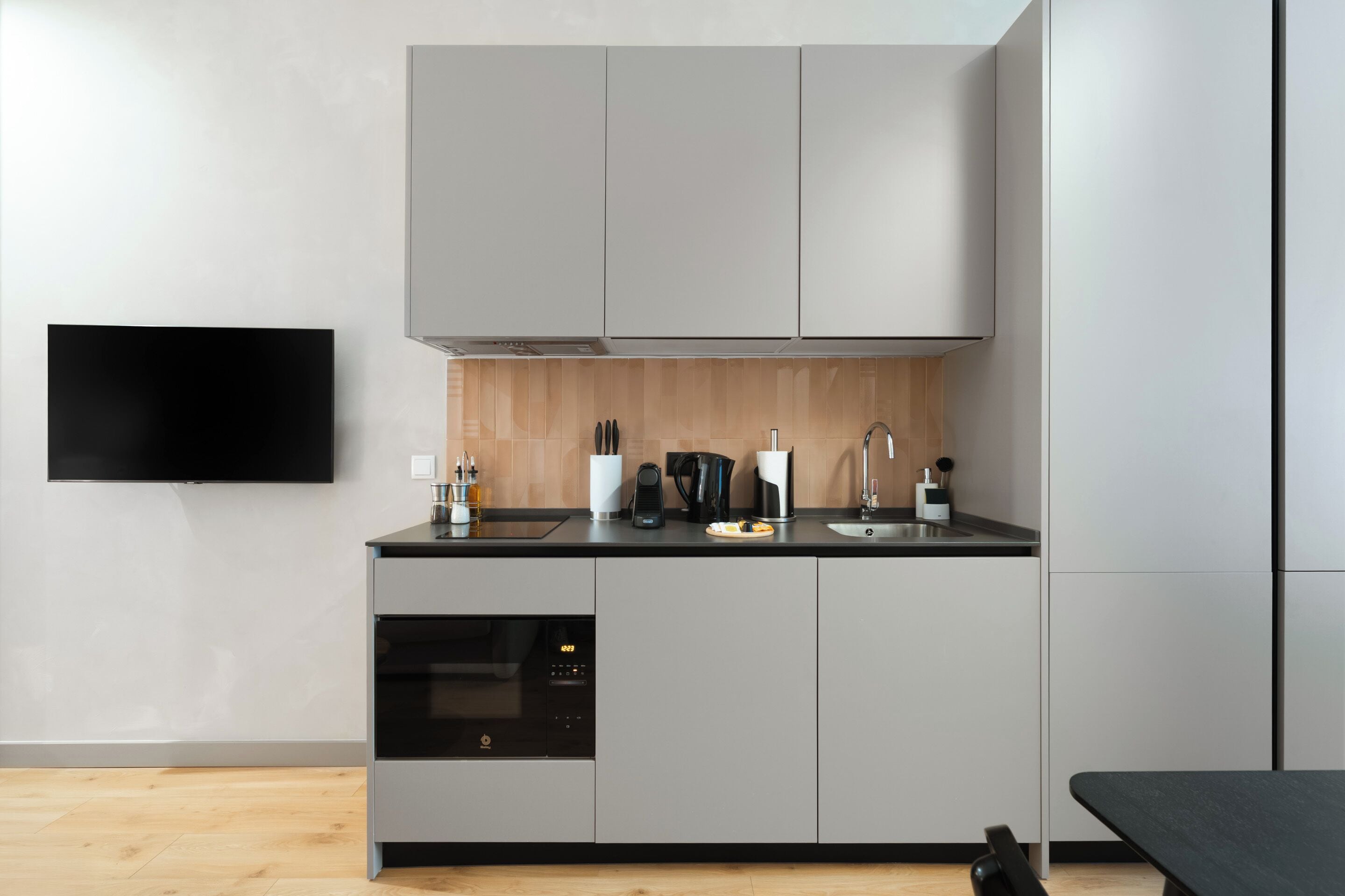 A modern kitchen with grey cabinets, a black oven, a sink, and a black countertop.