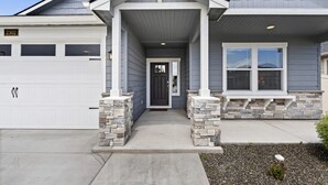 A two-story house with a covered front porch, stone pillars, and a garage door.
