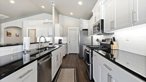 A modern kitchen with white cabinets, black countertops, stainless steel appliances, and recessed ceiling lights.