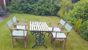 A garden with a wooden table and chairs, surrounded by greenery.