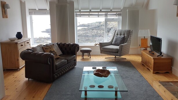 A living room with a sofa, armchair, glass coffee table, and a TV on a wooden stand.