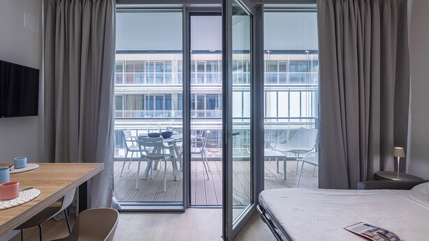 Une chambre d’hôtel avec un lit, un bureau et un balcon équipé de chaises.