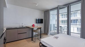 Une chambre d’hôtel moderne équipée d’un lit, d’une petite kitchenette, d’un coin repas et d’un balcon offrant une vue sur la ville.