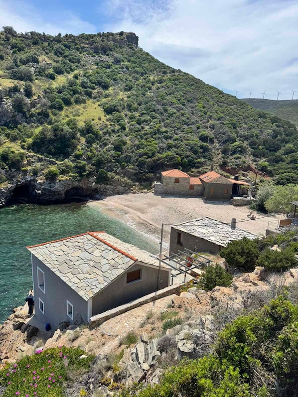 A coastal village with stone buildings, a beach, and a mountainous backdrop.