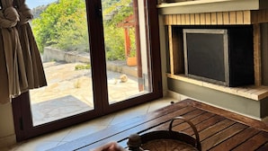 A room with a sliding glass door leading to an outdoor area, a fireplace, and a wooden floor. - Villa Apanemia Tsakaioi (Karystos)