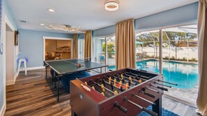Une pièce équipée d’un baby-foot, d’une table de billard et d’un coin salon avec un canapé et des fauteuils.