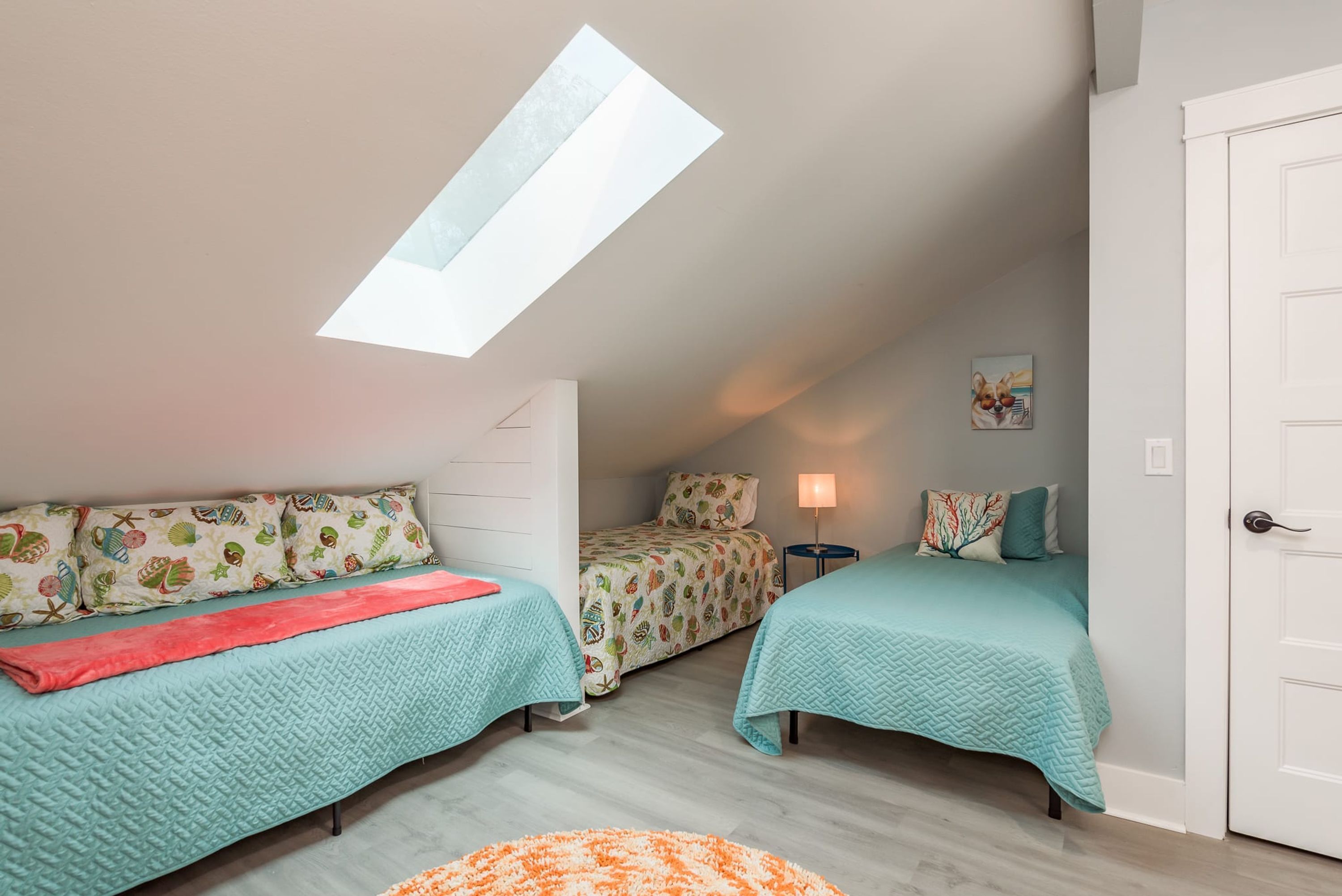A bedroom with two beds, a skylight, a lamp, and a door.