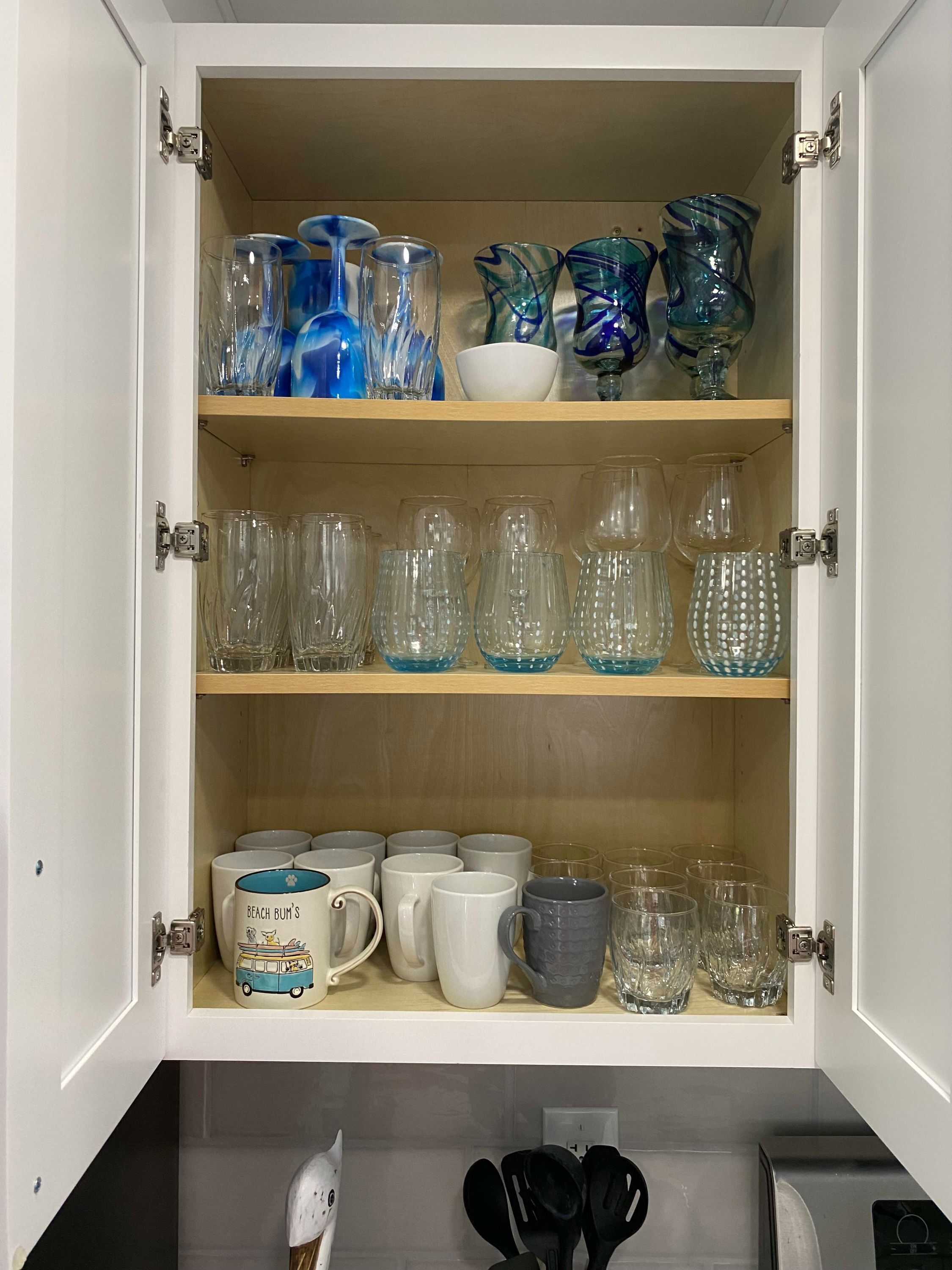 Et skab med hylder fyldt med forskelligt glas og krus.