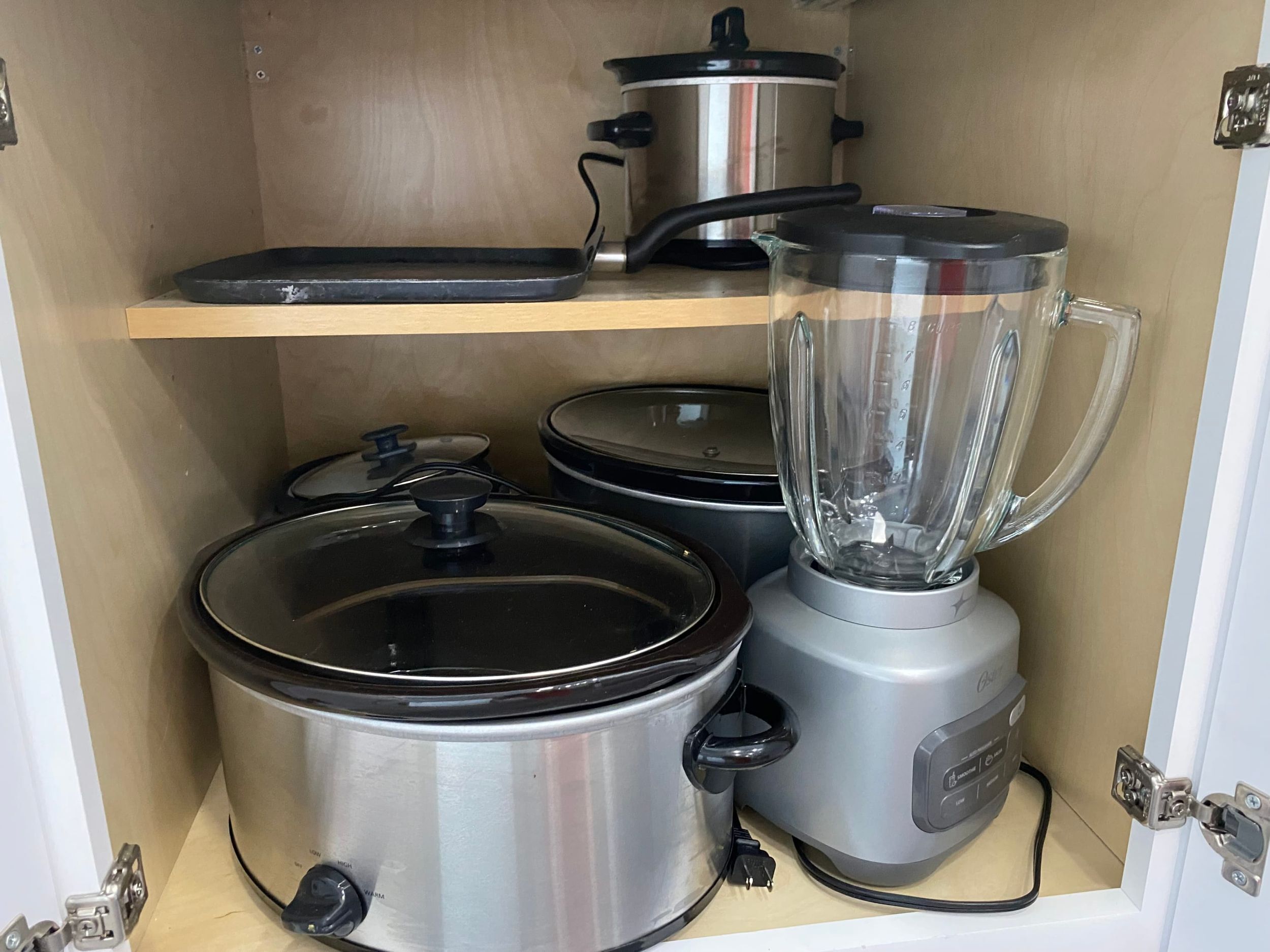 A kitchen with stainless steel appliances, including a blender, slow cooker, and a pot on a shelf.