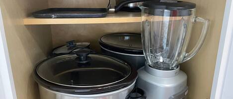 A kitchen with stainless steel appliances, including a blender, slow cooker, and a pot on a shelf.