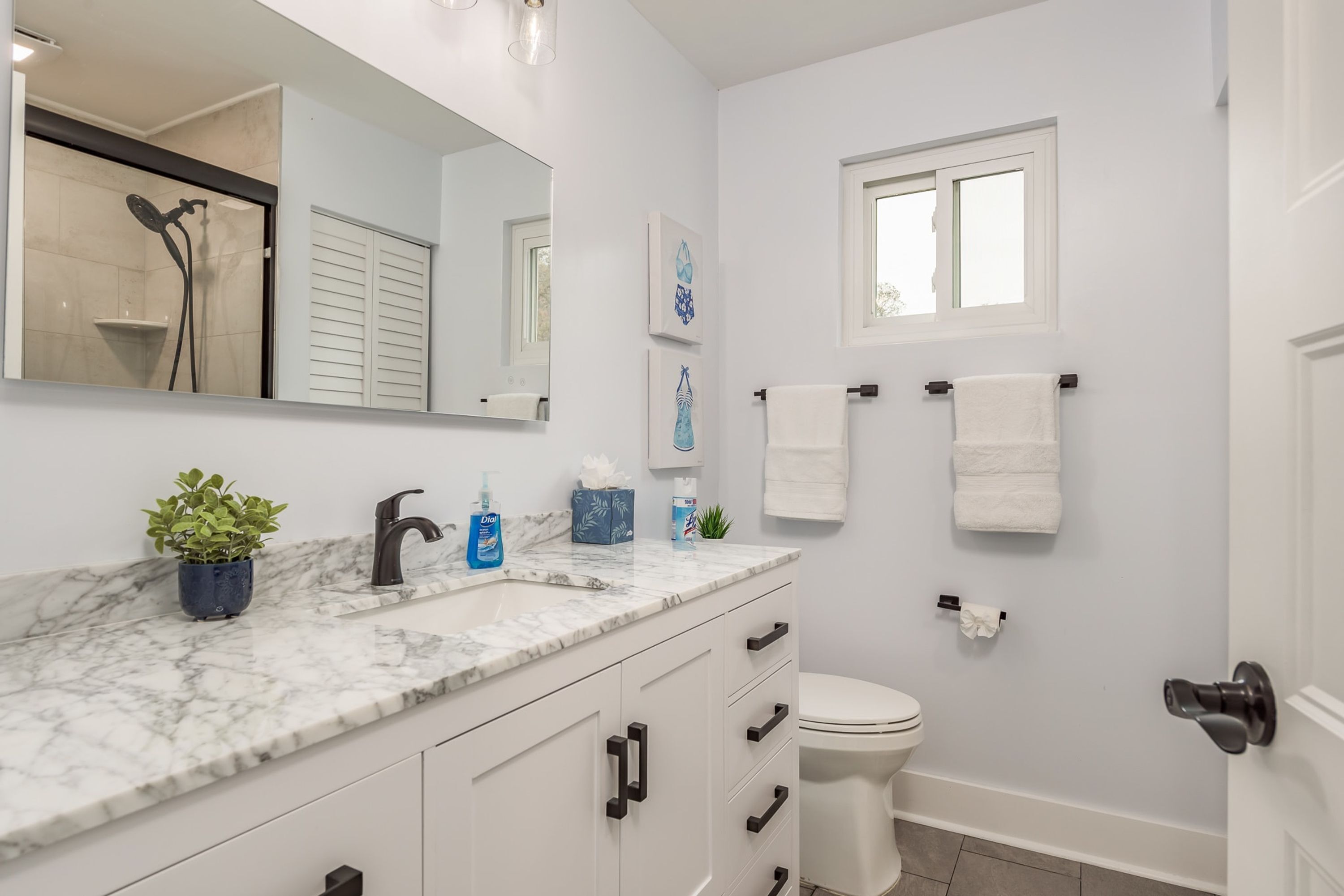 A modern bathroom with a marble countertop, a toilet, a shower, and a window.