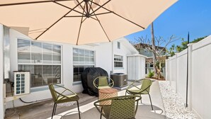 Un patio al aire libre con una mesa, sillas, una sombrilla grande y una parrilla.