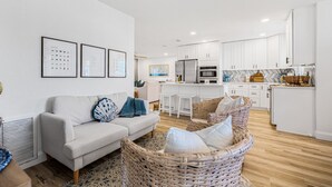A modern living room with a sofa and wicker chairs, a kitchen with white cabinets, and framed pictures on the wall. - Castaway Cottage Near IMG and Beaches (Bradenton)