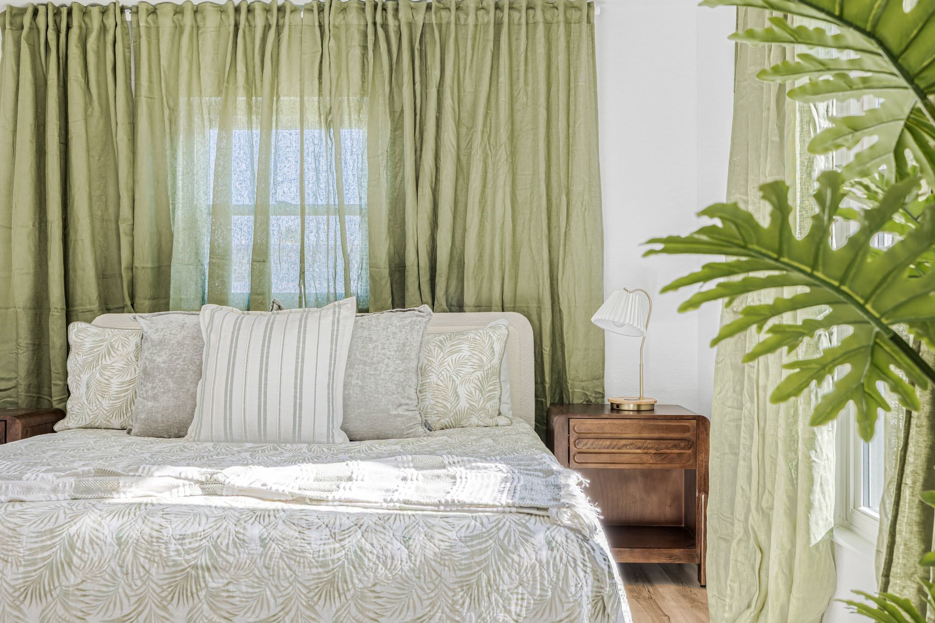 A bedroom with a bed, curtains, a nightstand, and a potted plant.