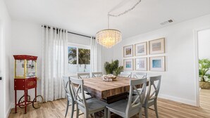 A dining area with a wooden table, grey chairs, a chandelier, and framed pictures on the wall. - Castaway Cottage Near IMG and Beaches (Bradenton)