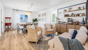 A modern living room with a sofa, wicker chairs, a dining table, and a kitchen area with shelves and appliances. - Castaway Cottage Near IMG and Beaches (Bradenton)