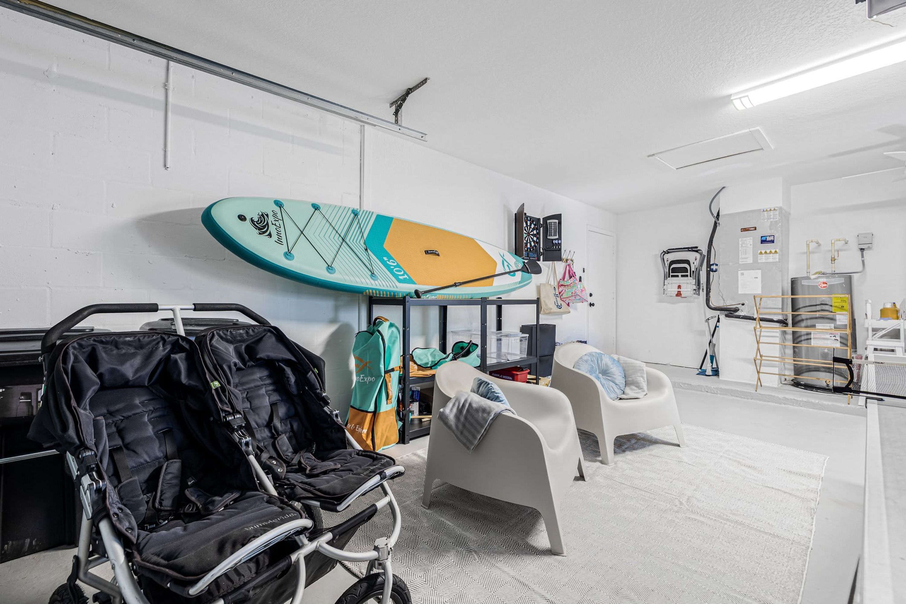 A room with a white brick wall, a surfboard, a stroller, a chair, and a water heater.