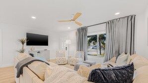A modern living room with a beige sofa, patterned armchairs, a flat-screen TV, and a ceiling fan. - Castaway Cottage Near IMG and Beaches (Bradenton)