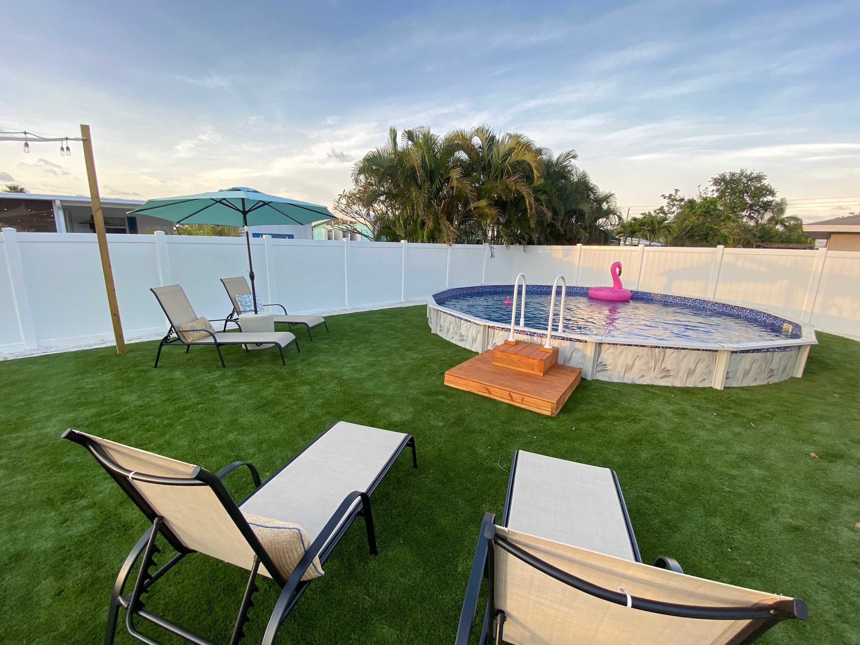 Un patio con césped artificial, una piscina y dos sillones de relax.