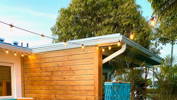 Eine Terrassengruppe im Freien mit einem Holztisch, gedeckt für ein Essen, umgeben von Korbstühlen und blauen Kissen.