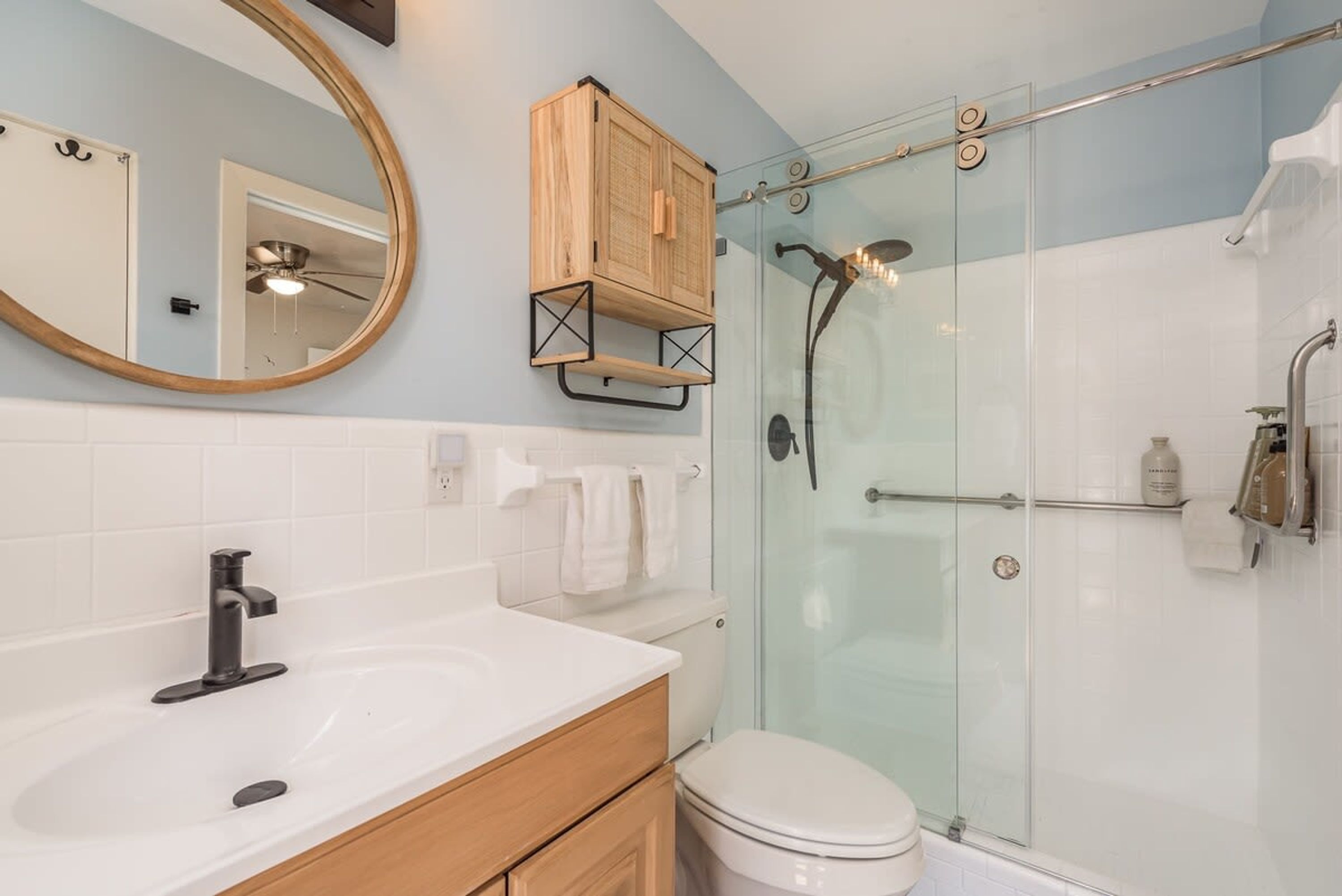Een badkamer met een wit wastafelmeubel, een spiegel, toilet en een douchecabine.