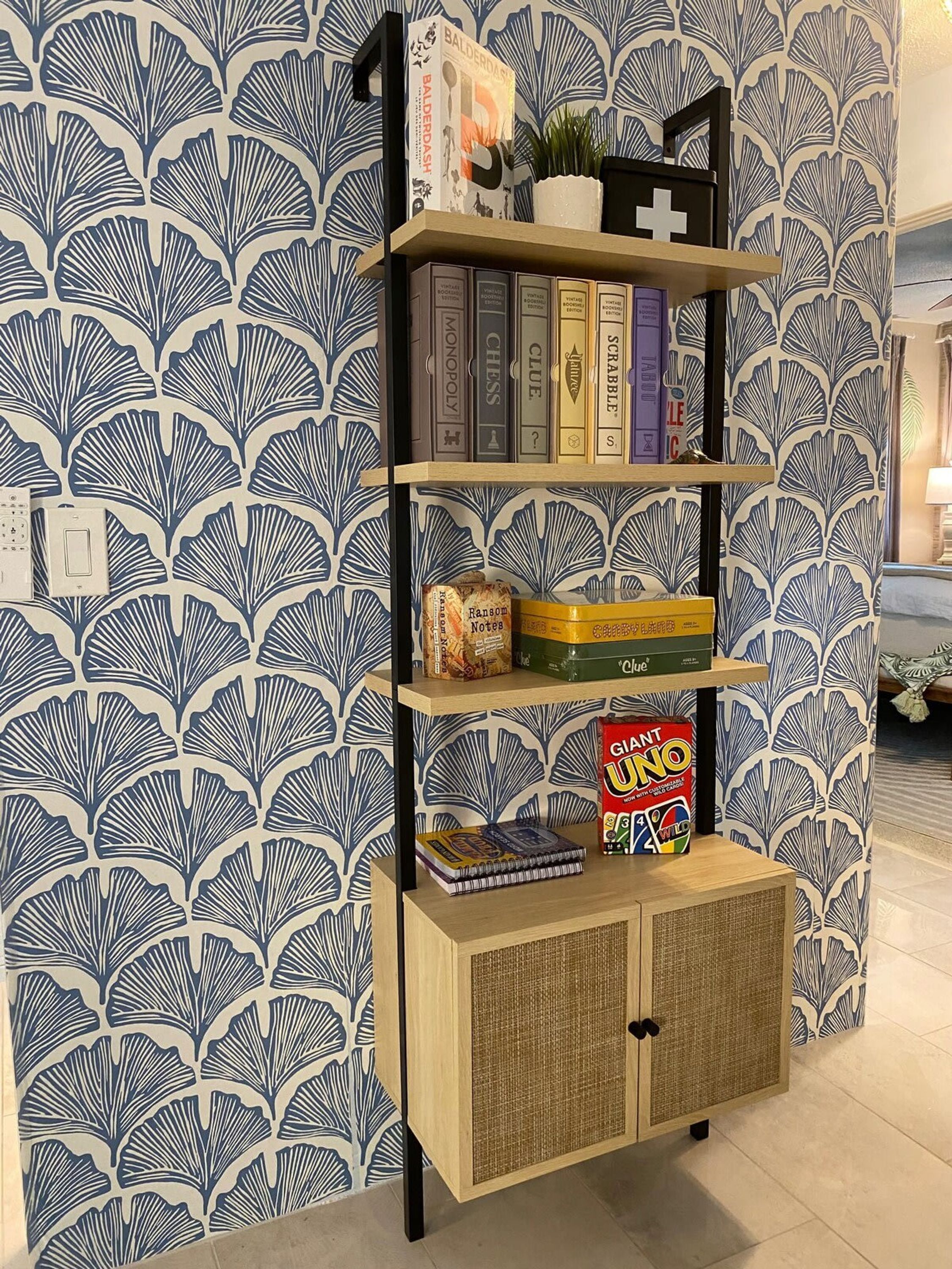 A bookshelf with various books and board games, set against a patterned wallpaper.