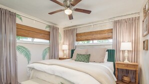 Ein Schlafzimmer mit einem Bett, zwei Nachttischen, einer Bank, einem Deckenventilator und Vorhängen.