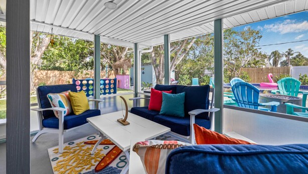 A covered outdoor seating area with a blue sofa, white coffee table, and colorful chairs.