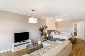 Una habitación de hotel moderna con una televisión de pantalla plana, un sofá, una cama, una planta en maceta y una mesita con lámpara.