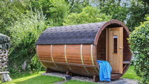 Un bâtiment en forme de tonneau, fait de bois, avec une porte, un banc et une serviette à l’extérieur.