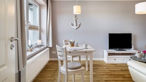 Une pièce moderne comprenant une table à manger, des chaises, un téléviseur et une fenêtre avec des rideaux.
