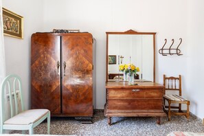 Una habitación con un armario de madera, un espejo, una silla y una pequeña mesa con flores.