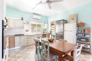 Une cuisine avec des meubles blancs, une table à manger, des chaises, un réfrigérateur et une bibliothèque.